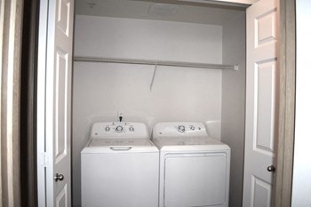 A washer and dryer side by side with a shelf above in a closet with accordion doors.